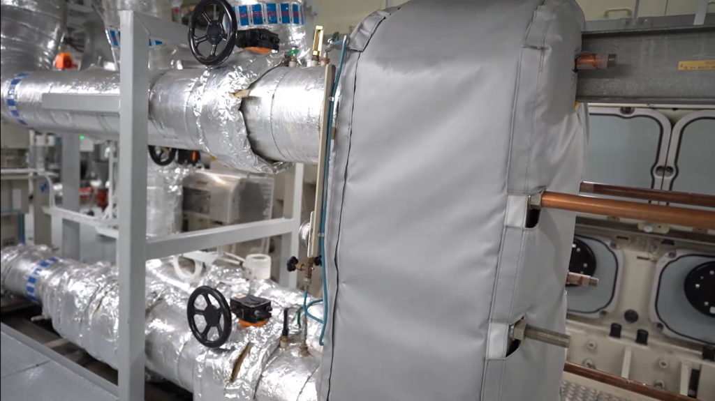 Close-up of a waste heat exchanger, featuring insulated piping and advanced energy recovery systems in a maritime environment.